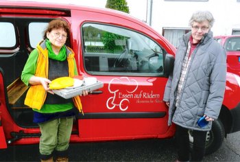 Aktion "Essen auf Rädern" Zwei Helferinnen stehen vor einem Auto der Aktion „Essen auf Rädern“ und bringen eine warme Mahlzeit zu einem Menschen, der sich nicht mehr selbst versorgen kann.