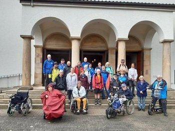 Menschen mit und ohne Rollstuhl vor einem Haus.