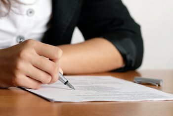 Eine junge Frau (man sieht nur den rechten Arm) schreibt etwas auf ein Blatt Papier